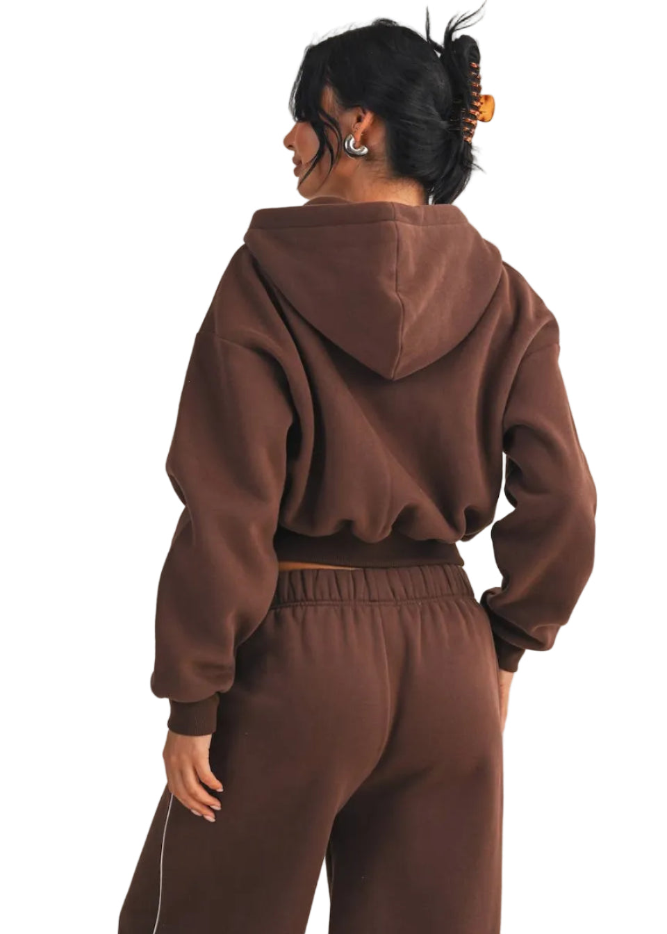 Person wearing a brown hoodie and pants set on a beige background