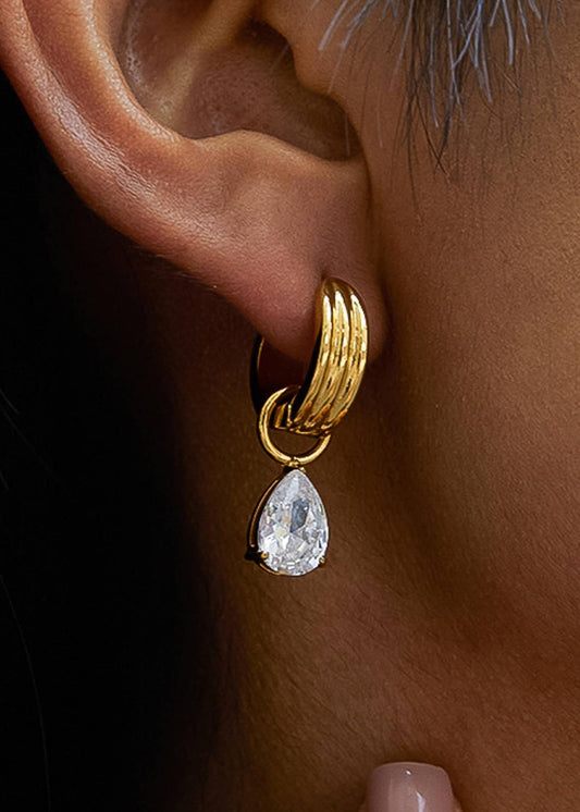 Gold hoop earring with a teardrop-shaped gemstone worn by an ear.