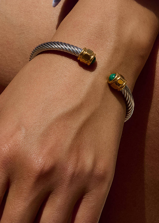 Close-up of a wrist wearing a silver and gold bracelet with a green gemstone on a brown background