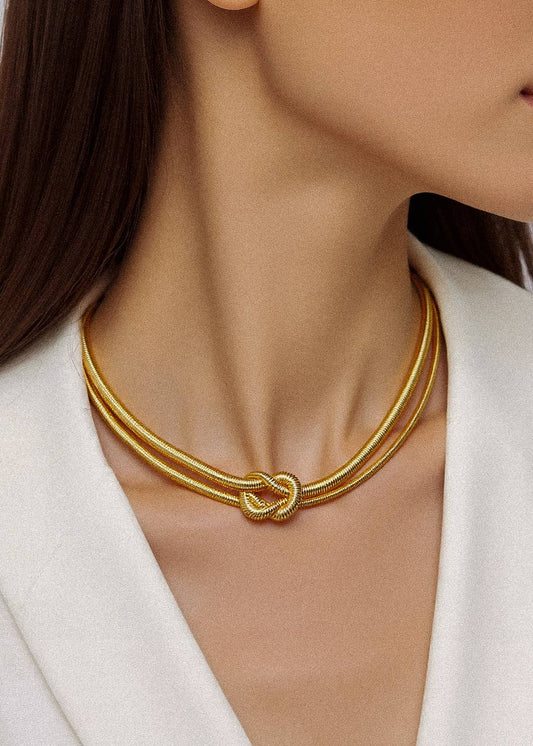 Gold necklace worn by a person against a neutral background