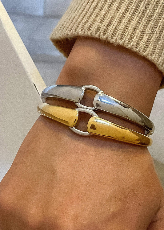 A person's wrist wearing a Modern Hoop Bangle with gold and silver colors.