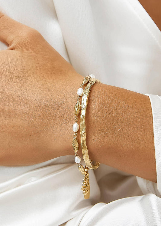 Gold bracelet with pearls on a wrist against a white background