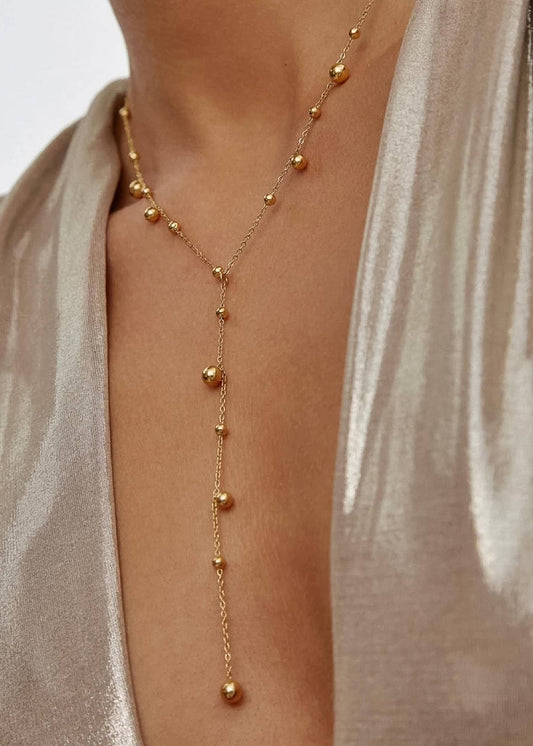 Gold necklace with beads on a person wearing a light-colored garment