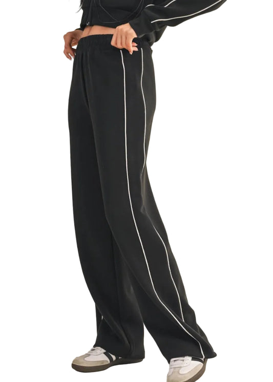 Black pants with white stripes worn by a person on a beige background