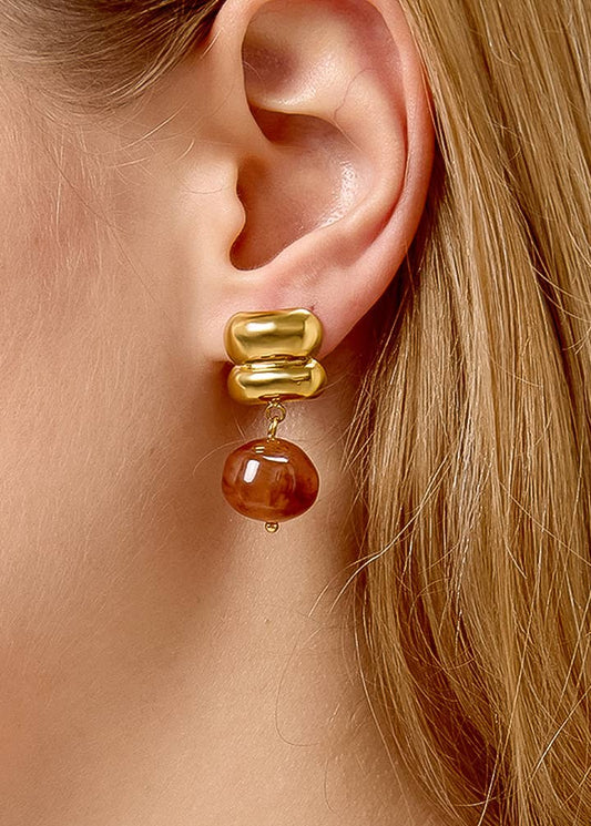 Gold and brown earring worn by a person with blonde hair.