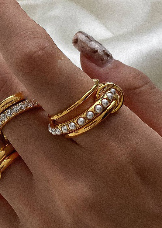 Gold ring with pearl accents on a hand against a neutral background