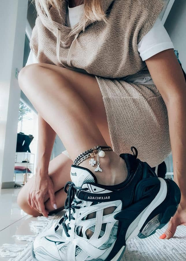 Person wearing white and black sneakers with colorful bracelets, sitting indoors.
