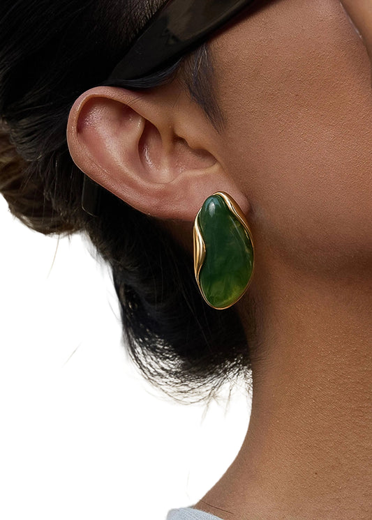 Close-up of a person wearing a green earring with gold setting outdoors.