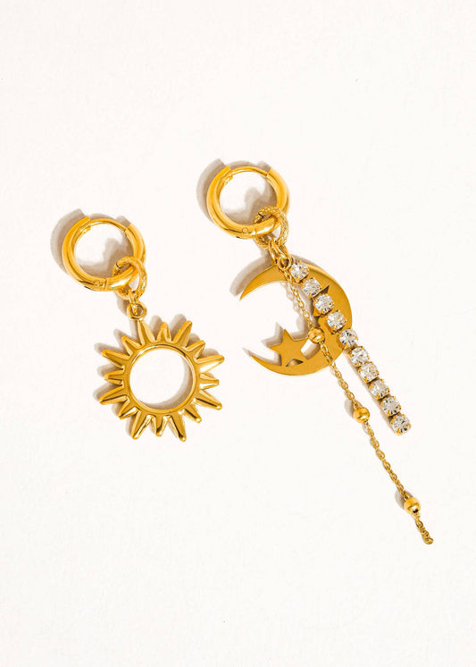 A pair of earrings, one shaped like a sun with a gold plating and rhinestones, and one shaped like a moon with a gold plating and a chain detail.