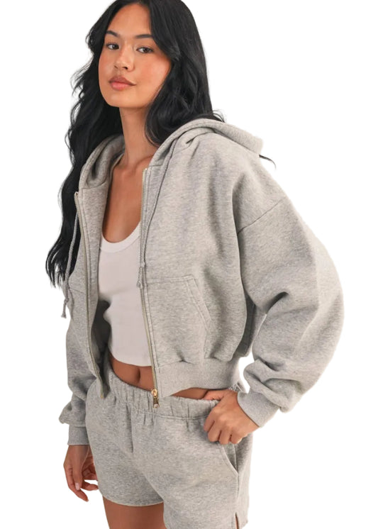 Woman wearing a gray hoodie and shorts set on a beige background