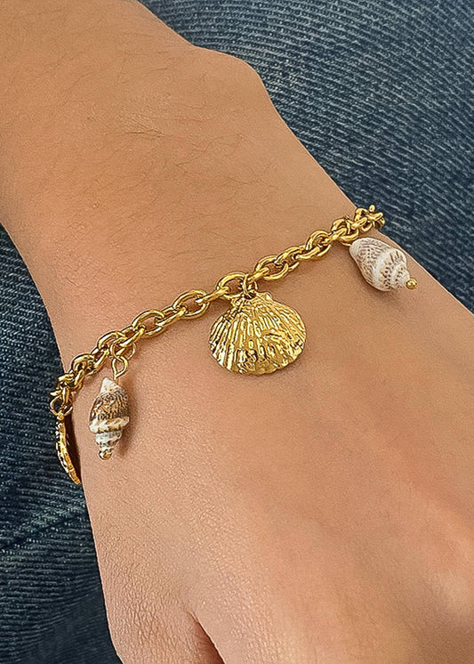 Gold bracelet with shell charms on a wrist against a denim background
