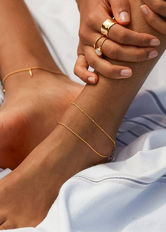 Close-up of a person's feet with gold anklets and rings on a light background
