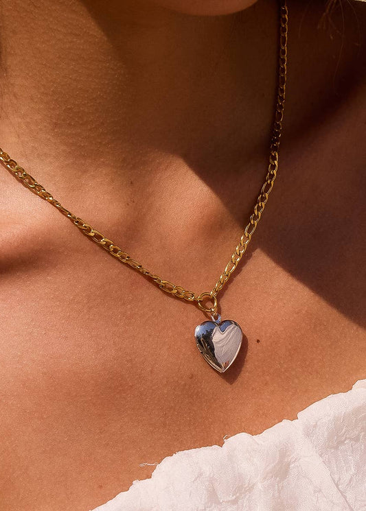 Gold chain necklace with a heart-shaped pendant on a person's neck.