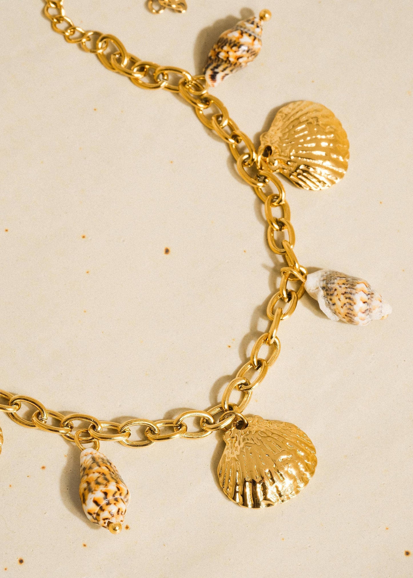 Gold bracelet with shell charms on a beige background