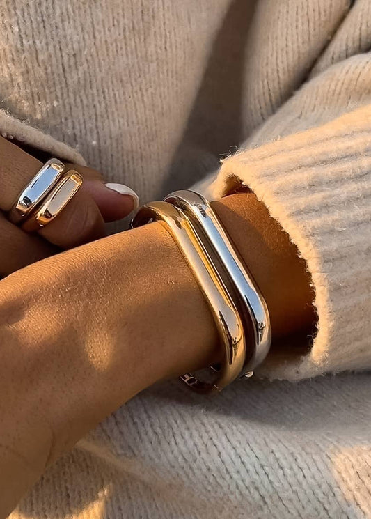 Close-up of a wrist wearing gold bracelets and rings against a neutral background