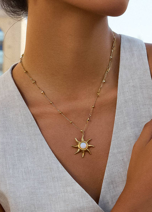 Gold necklace with a sun pendant worn by a person in a light gray sleeveless top.