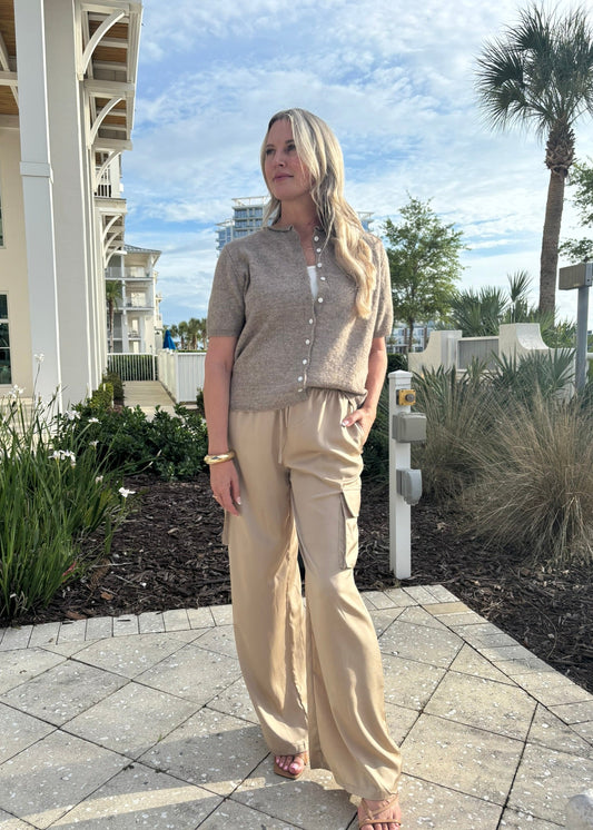 Woman in beige outfit standing outdoors with buildings and palm trees in the background