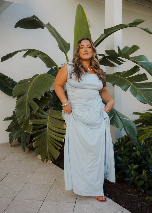 Woman in a light blue dress standing in front of large green leaves