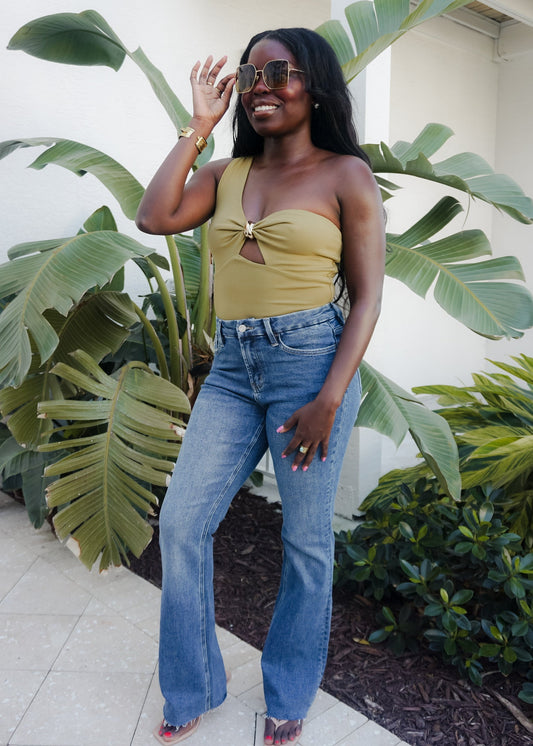 Woman in yellow top and blue jeans standing in front of green plants