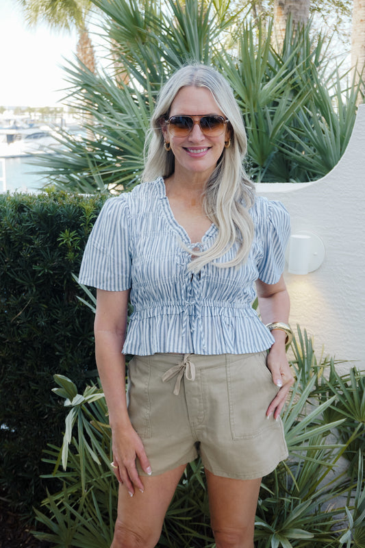 Woman wearing a striped shirt and shorts standing outdoors with plants in the background