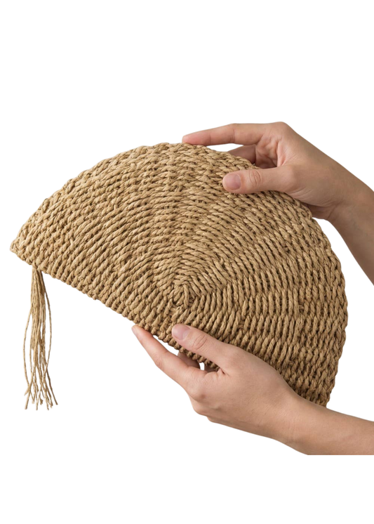 Hand holding a woven clutch bag with a tassel on a white background