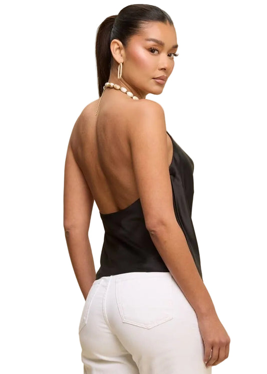 Woman wearing a black open-back top and white pants on a beige background