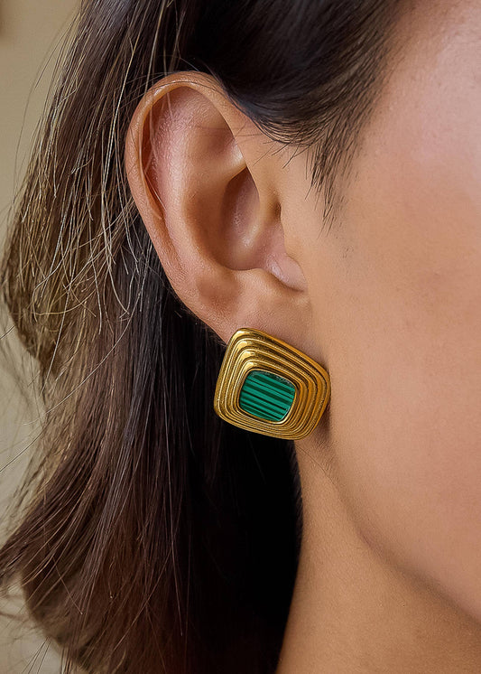 Gold and green earring worn by a person with brown hair.