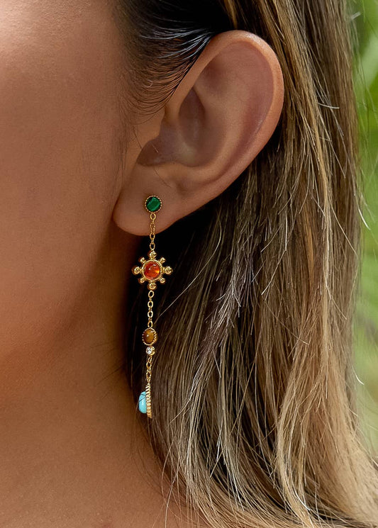 Close-up of a person wearing a gold earring with colored stones.