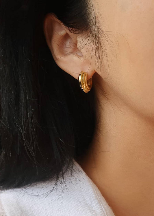 Close-up of a person wearing gold hoop earrings with a blurred background