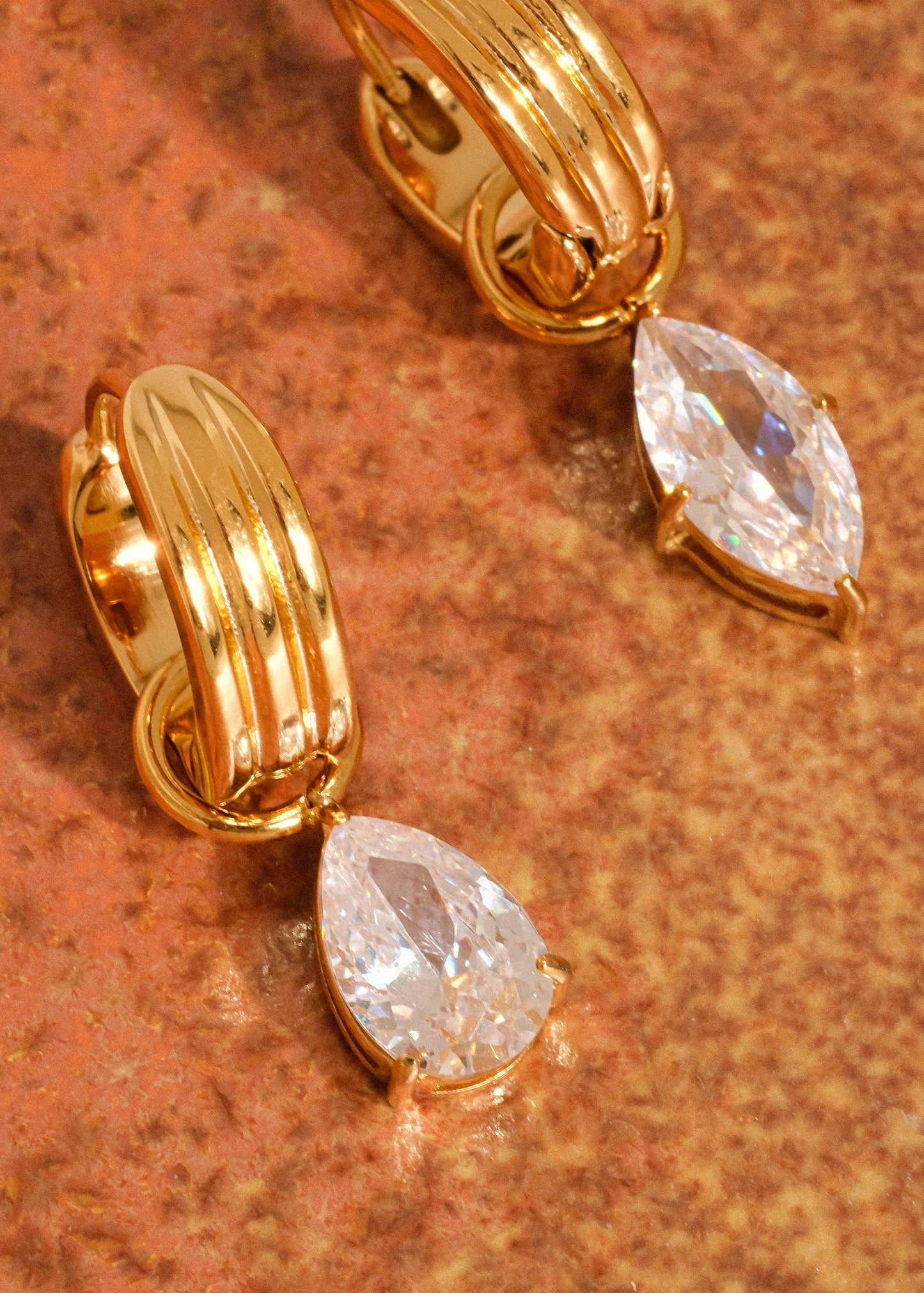 Gold earrings with teardrop-shaped crystals on a textured brown surface