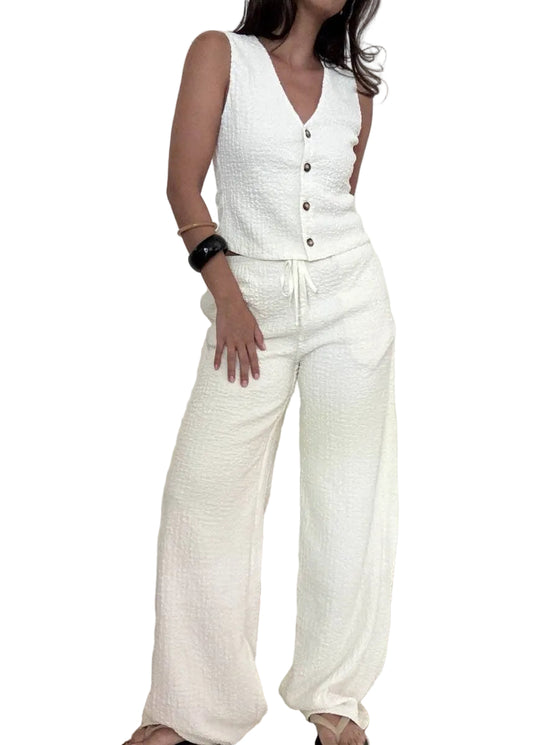 Person wearing a white sleeveless top and wide-leg pants against a plain background