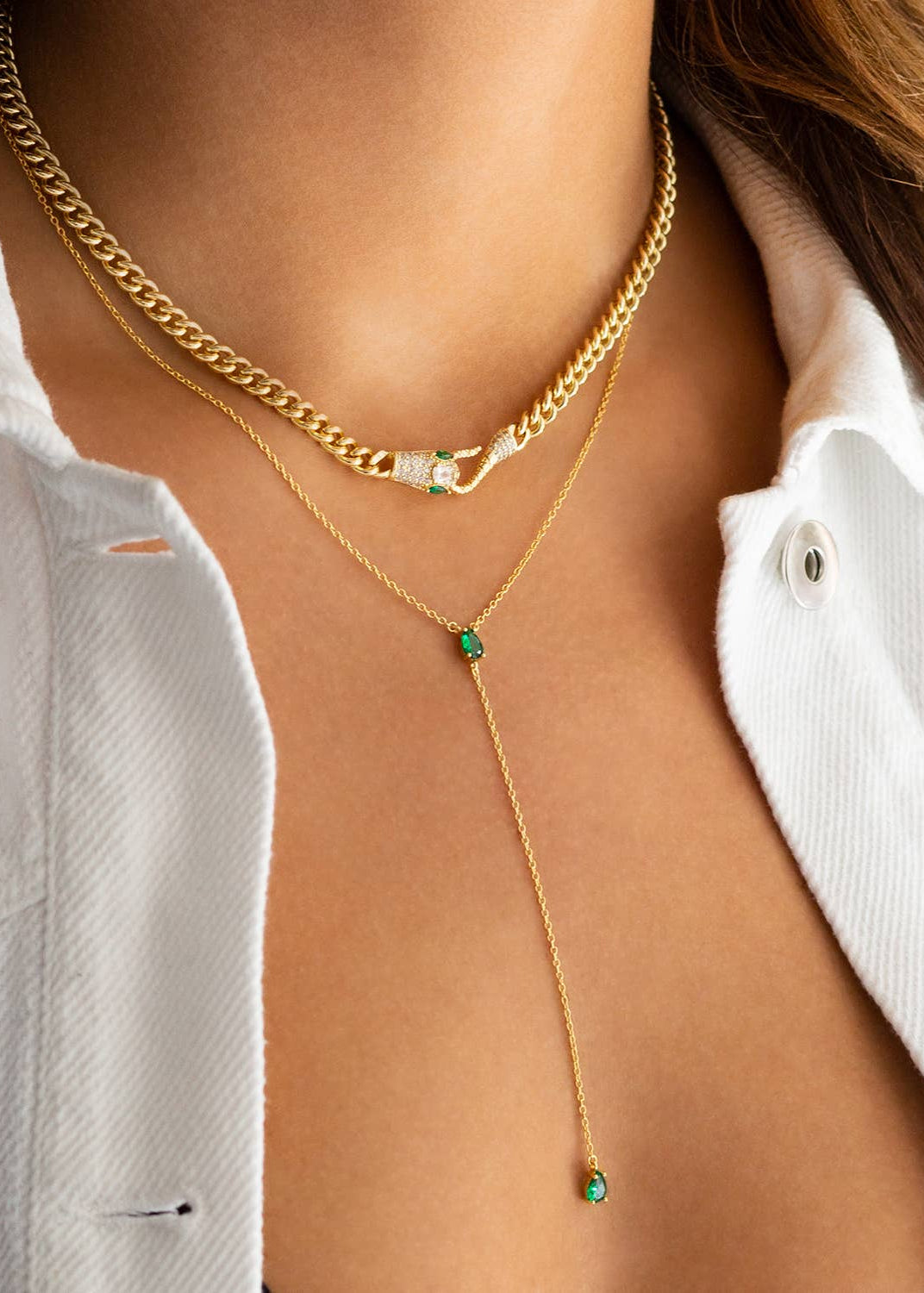 Gold necklace with green gemstones worn by a person against a neutral background