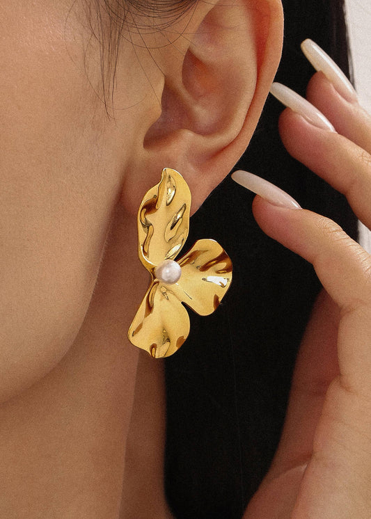 Gold leaf-shaped earring worn by a person with a blurred background