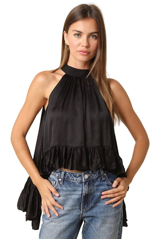A woman modeling a black halter-neck ruffled top paired with blue jeans, standing against a solid beige background.