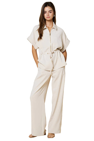 Woman wearing a beige outfit with a matching jacket and pants on a beige background