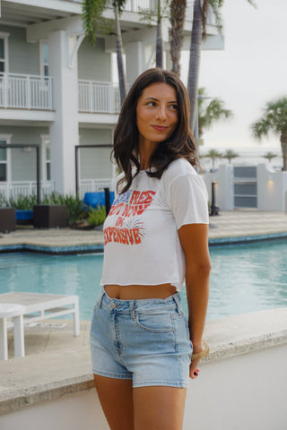 Woman standing by a pool wearing a white t-shirt with red text and denim shorts.