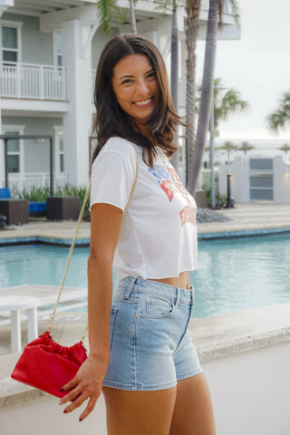 Woman in white t-shirt and denim shorts standing by a poolside.