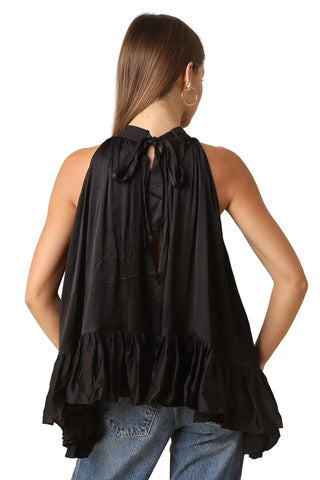 A woman shown from the back wearing a black sleeveless halter top with a tie-back neckline and ruffled hem, paired with blue jeans against a plain beige studio background.