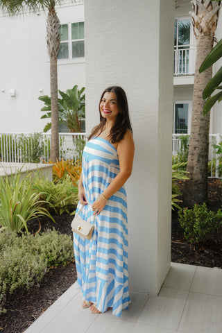 Woman in a blue and white striped dress standing outdoors with palm trees and a building in the background.
