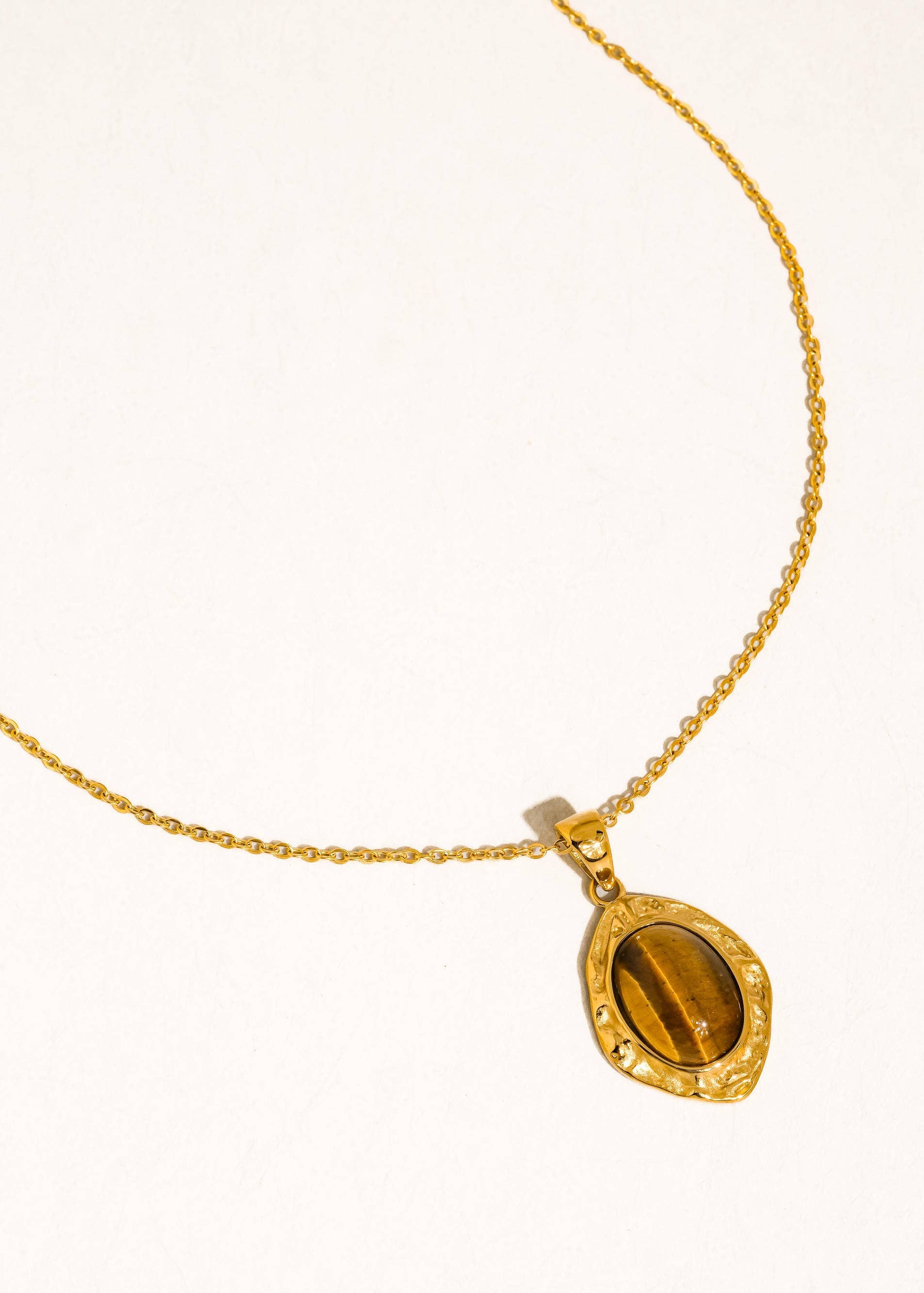 Gold necklace with a tiger's eye pendant on a white background
