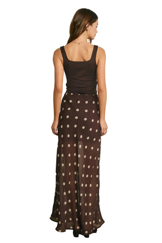 Woman wearing a brown tank top and polka dot skirt against a plain background