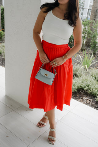 Woman wearing a white top and red skirt holding a small handbag.