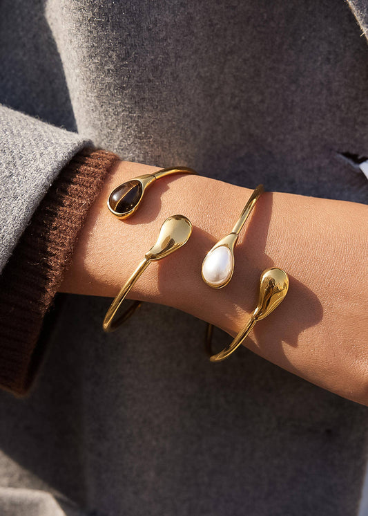 Gold spoon-shaped bracelets on a wrist with a neutral background