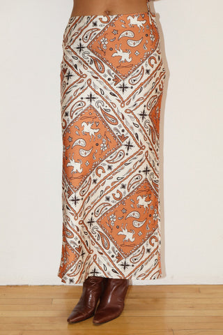 Person wearing a patterned skirt with orange and white design on a plain background