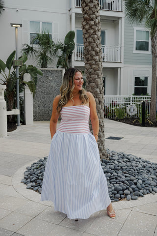 Woman in a striped dress standing in front of a building with palm trees.