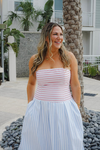 Woman in a striped dress standing outdoors with palm trees and a building in the background