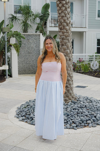 Woman in a striped top and light blue skirt standing in front of a palm tree and building.