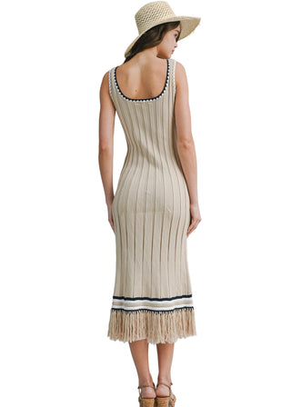 Woman wearing a beige ribbed dress with fringe details on a plain background
