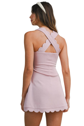 Woman wearing a light pink dress with a scalloped hem on a plain background