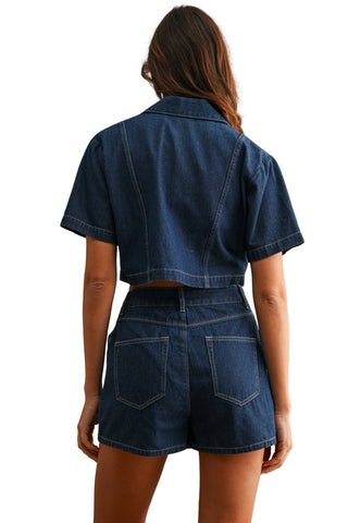 A woman shown from the back wearing a dark blue denim short-sleeve cropped jacket and matching high-waisted denim shorts against a neutral beige background.